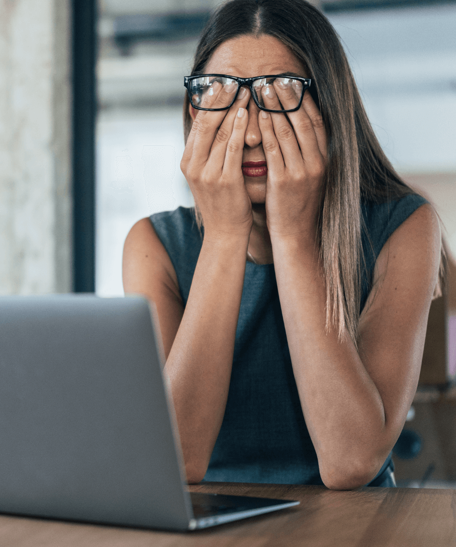 Tired woman with glasses covering her face, expressing fatigue and stress, sitting at a desk with a laptop, reflecting themes of low energy and hormonal imbalance.