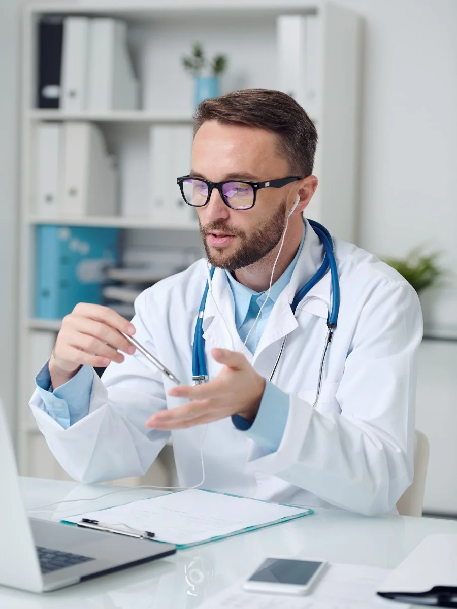 Medical expert in a white coat consulting with a patient, discussing wellness treatments, including hormone therapy, using a laptop and pen.