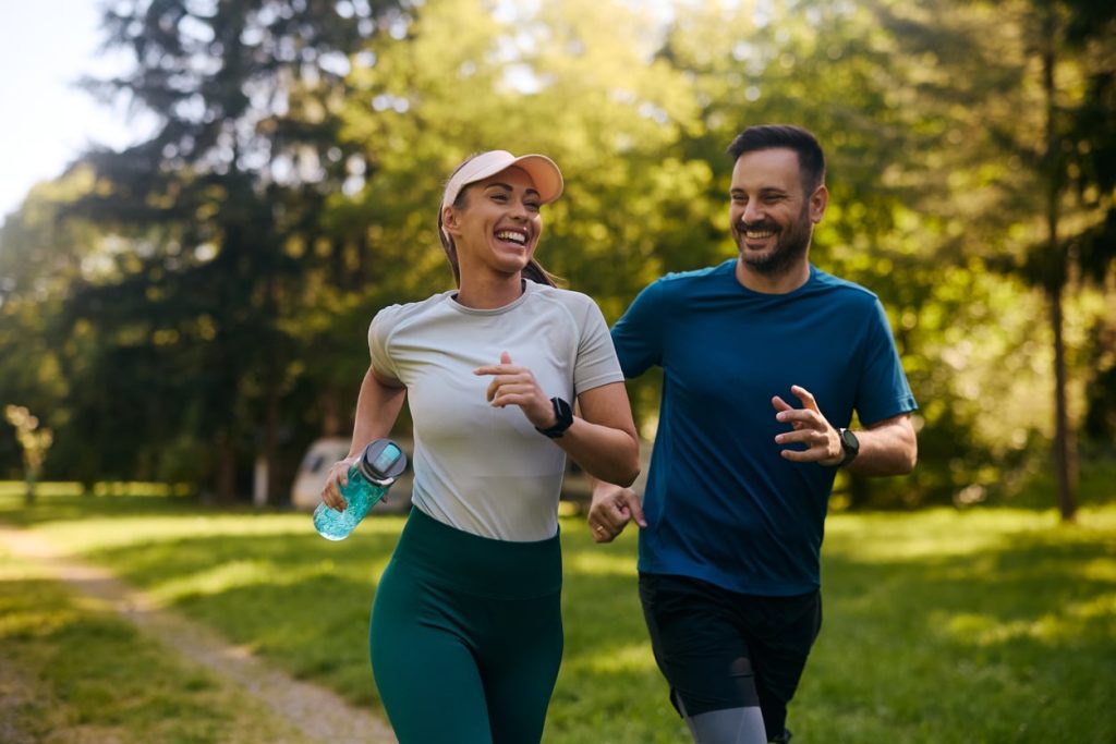 Happy couple jogging together in a green park, promoting energy and vitality, relevant to wellness and hormone therapy at CHS MedSpa.